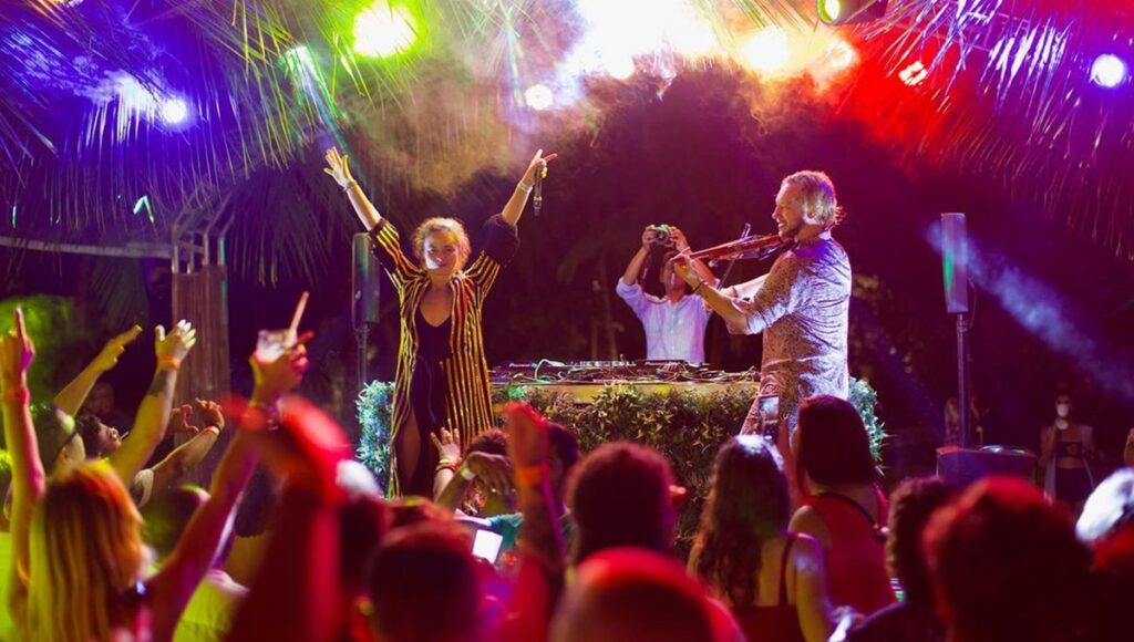 Sinop sahil partisi, kumsalda DJ performansı ve keman eşliğinde eğlenen turistler.